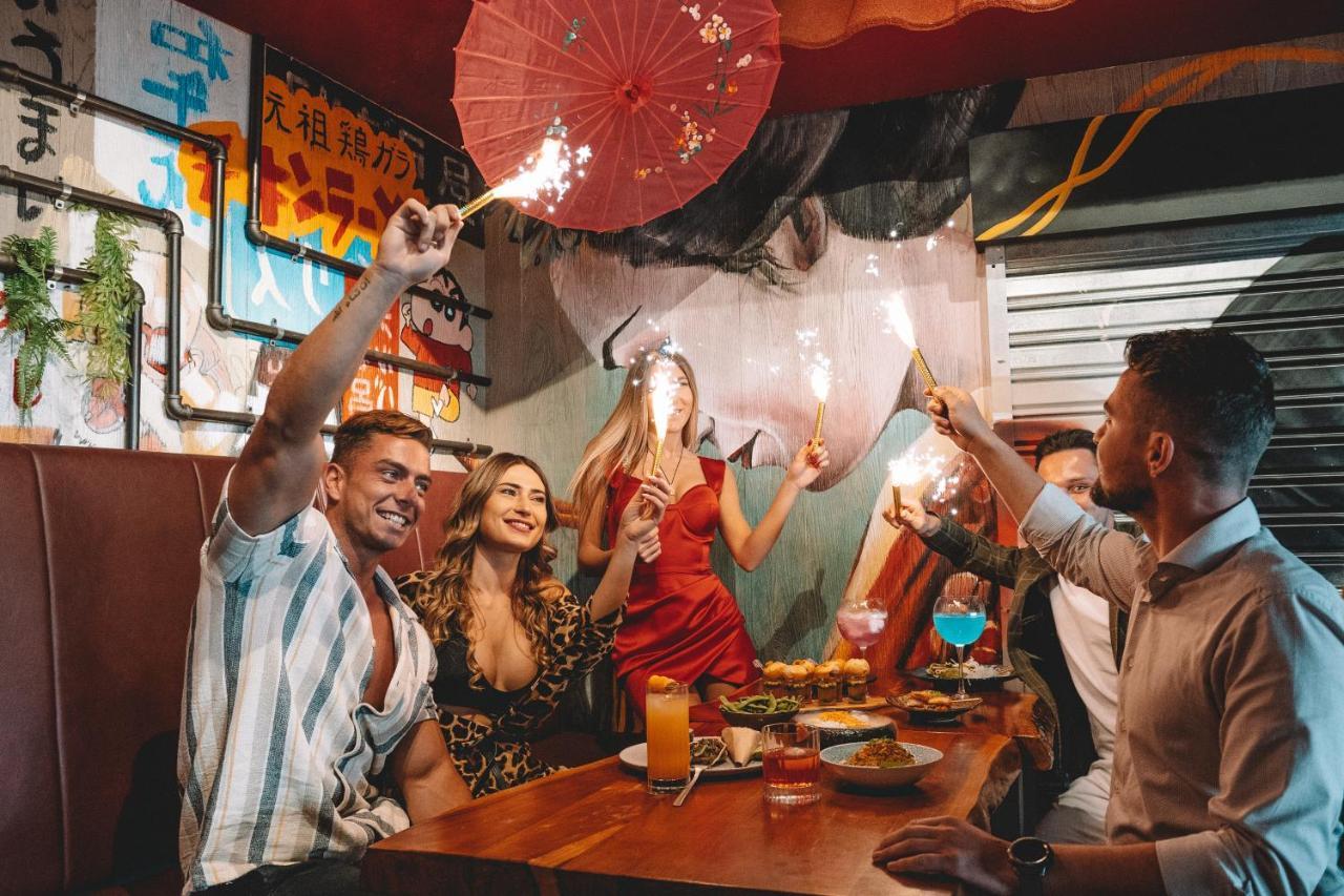 Five Jumeirah Village ดูไบ ภายนอก รูปภาพ The photo depicts a lively gathering at a dining table where several people are celebrating. There are four individuals: two men and two women. One of the women is wearing a red dress, while the other is dressed in a patterned outfit. They are holdin