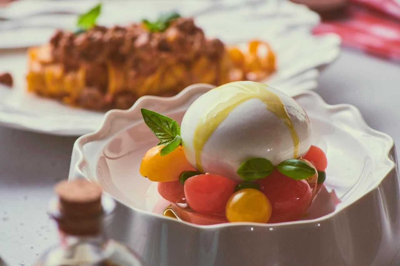 Five Jumeirah Village ดูไบ ภายนอก รูปภาพ The photo showcases a beautifully presented dish featuring a large ball of fresh mozzarella cheese, sitting atop a colorful assortment of small tomatoes. The tomatoes are a mix of red and yellow, creating a vibrant visual contrast. Fresh basil leaves