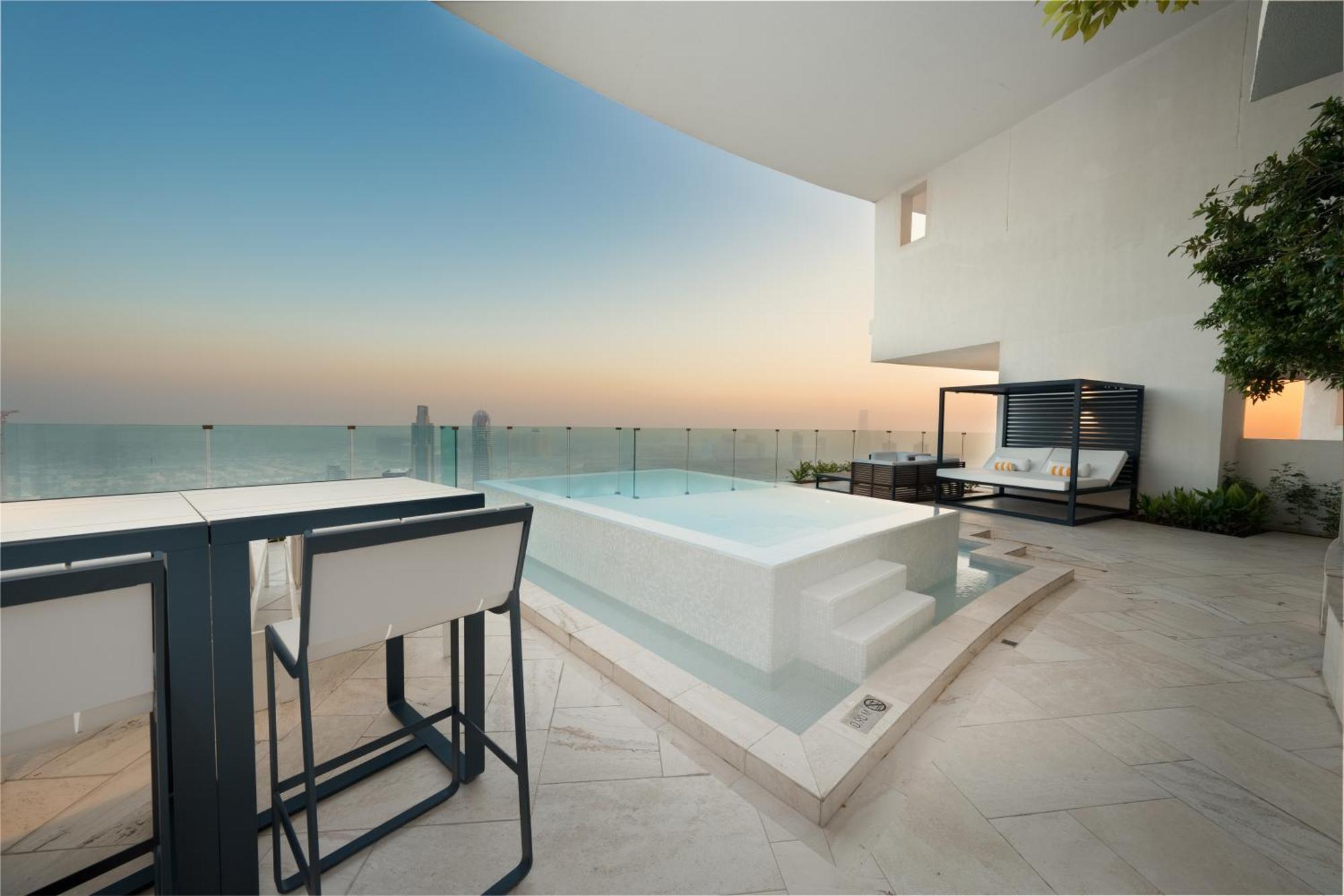 Five Jumeirah Village ดูไบ ภายนอก รูปภาพ The photo depicts a luxurious outdoor space featuring a small infinity pool or hot tub that overlooks a scenic view. There is a stylish seating area nearby with modern furniture, including a table and chairs. The surroundings have a minimalist design