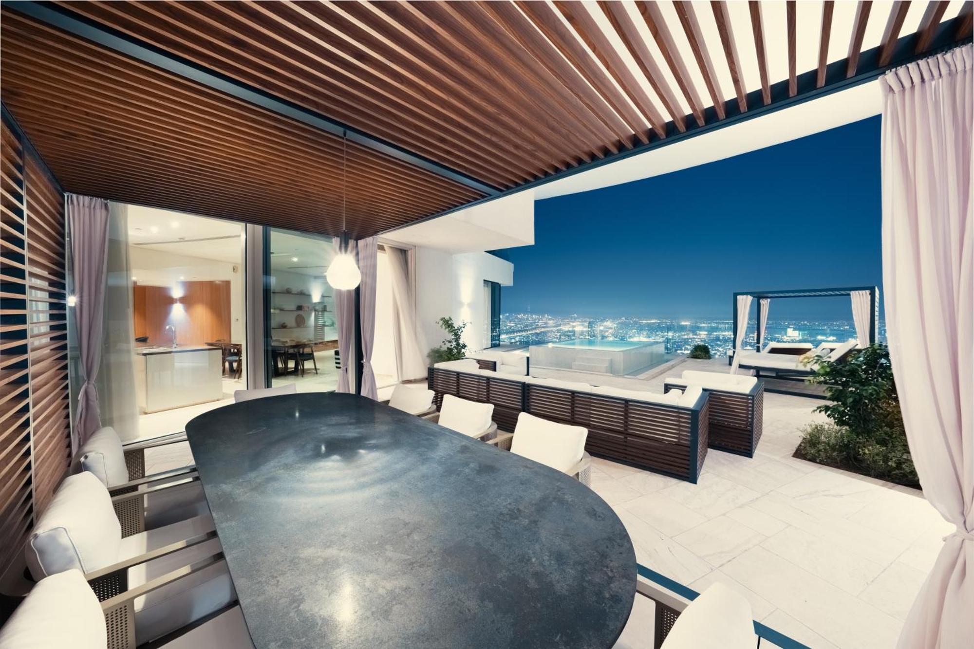 Five Jumeirah Village ดูไบ ภายนอก รูปภาพ The photo shows a modern outdoor dining area with a sleek, curved table surrounded by several chairs. It features a stylish wooden ceiling with slats, creating a shaded atmosphere. In the background, large glass doors lead to the interior of a house,
