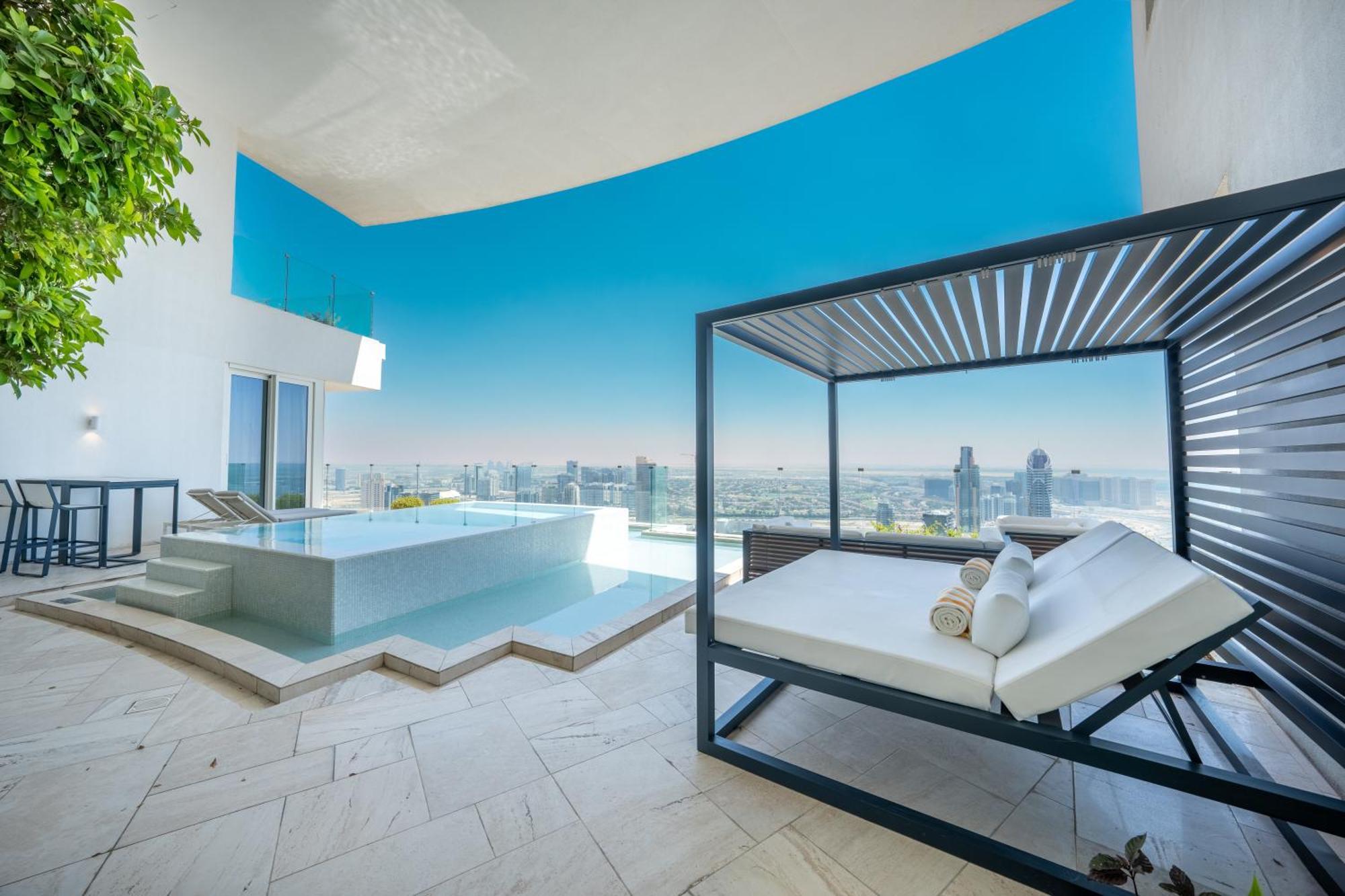 Five Jumeirah Village ดูไบ ภายนอก รูปภาพ The photo shows a luxurious outdoor space that features a modern infinity pool and a stylish lounging area. The pool appears to be surrounded by sleek stone tiles, creating a beautiful contrast with the bright blue sky above. There is a contemporary 