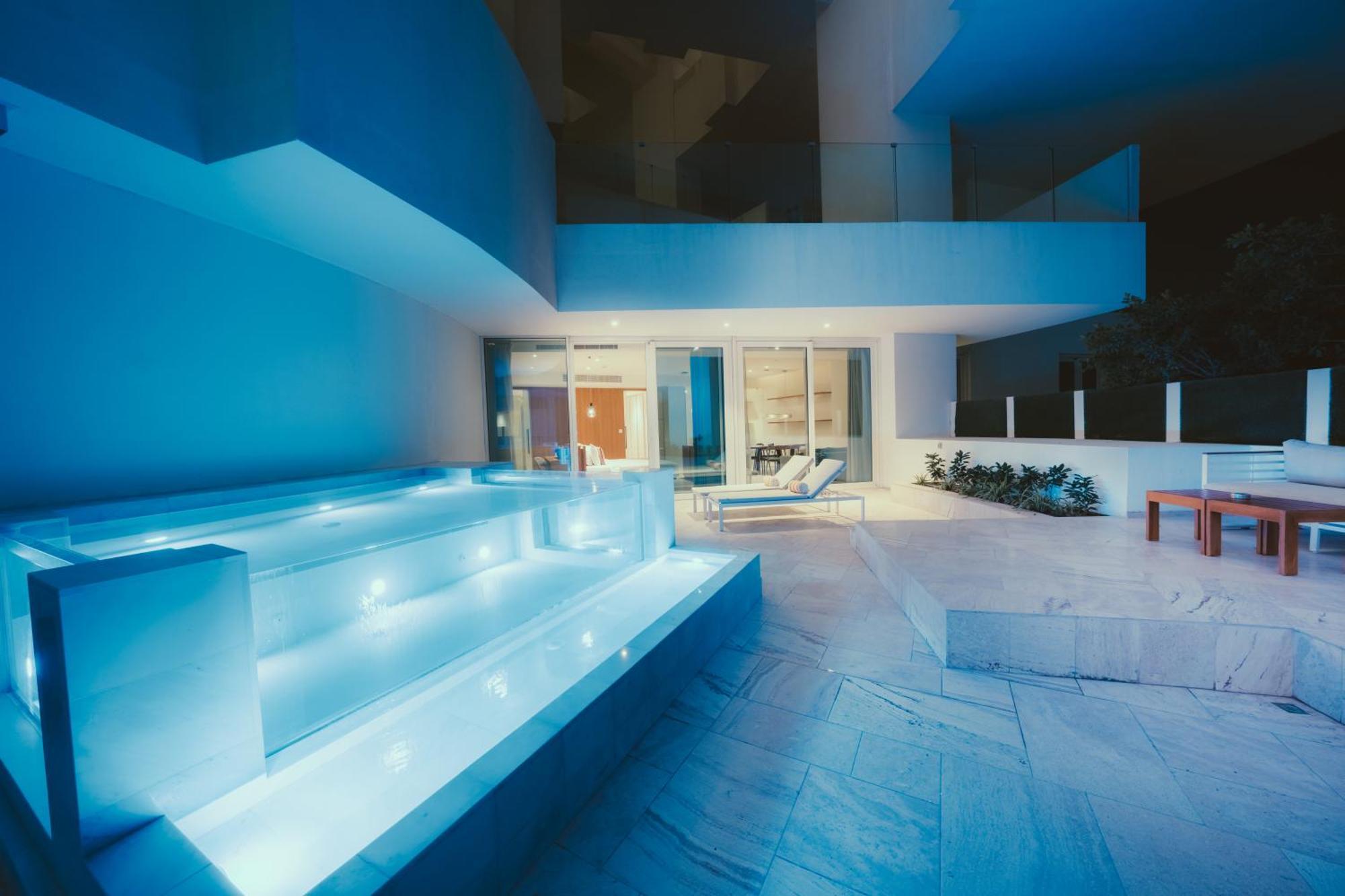 Five Jumeirah Village ดูไบ ภายนอก รูปภาพ The photo shows a modern outdoor area, likely part of a contemporary home. It features a stylish, illuminated staircase leading down to a pool or water feature, with soft blue lighting that creates a serene atmosphere. In the background, large glass 