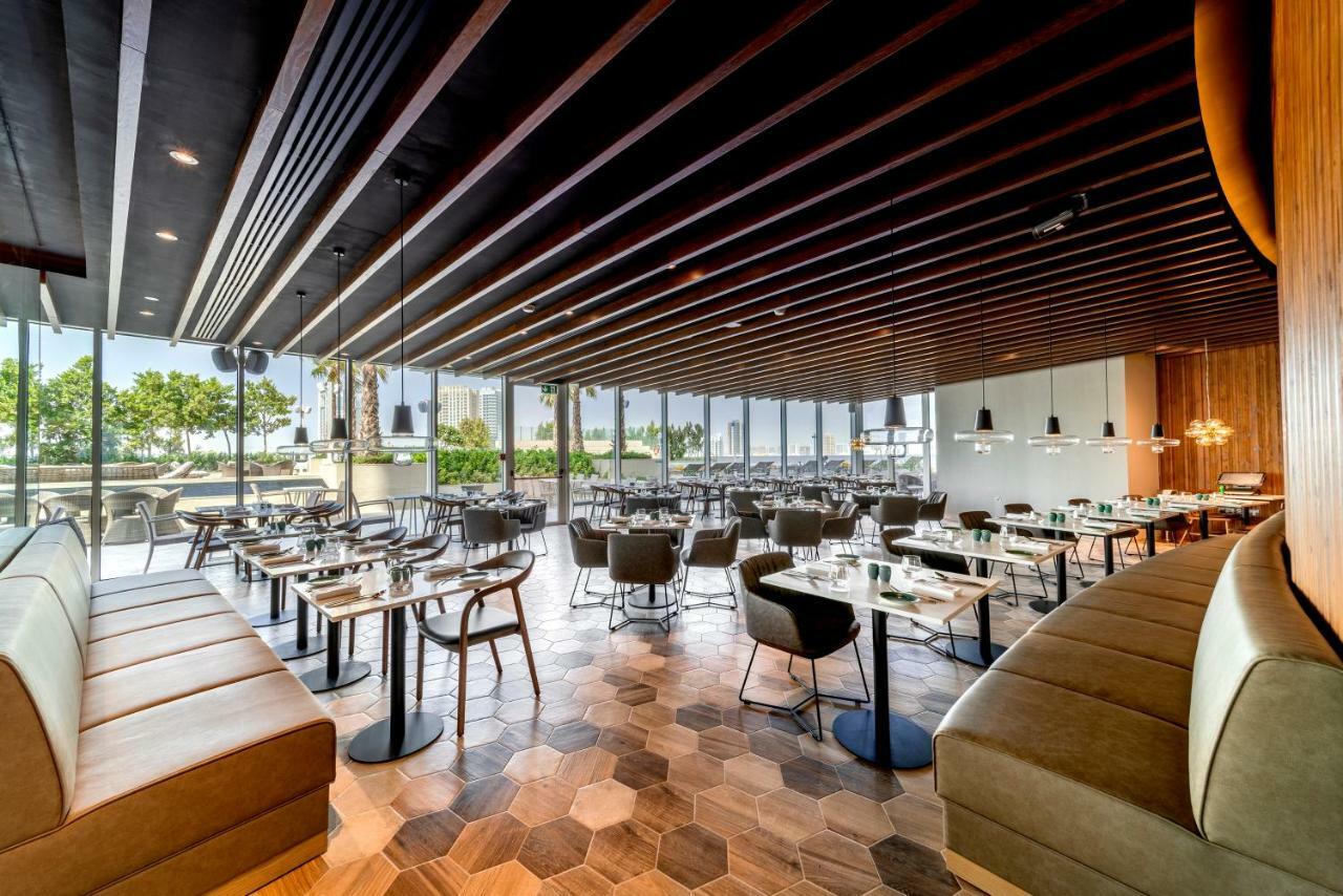 Five Jumeirah Village ดูไบ ภายนอก รูปภาพ The photo shows the interior of a modern restaurant. It features a spacious layout with a combination of wooden and tiled flooring, characterized by hexagonal tiles. The ceiling has a modern design with wooden beams that add a sophisticated touch. Th